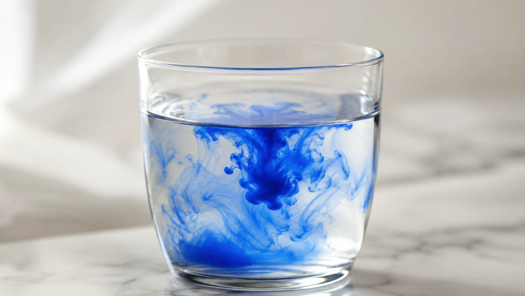 Goutte de bleu de méthylène se dissolvant dans un verre d'eau, illustration des propriétés de ce colorant synthétique
